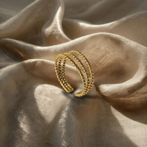 Triple twisted band ring in handcrafted gold-plated bronze, displayed centered on a linen-textured background with soft daylight and subtle shadows