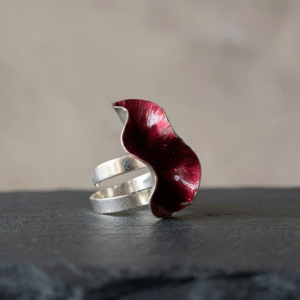 Adjustable silver statement ring with a red sculptural leaf design on a natural background.