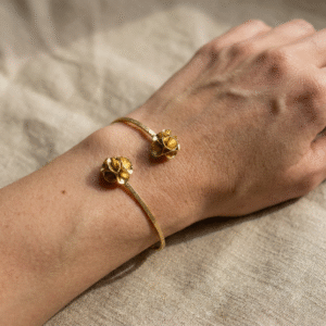Gold-plated bronze Twin Bloom Bracelet with two sculptural flower ends on a dark stone background.