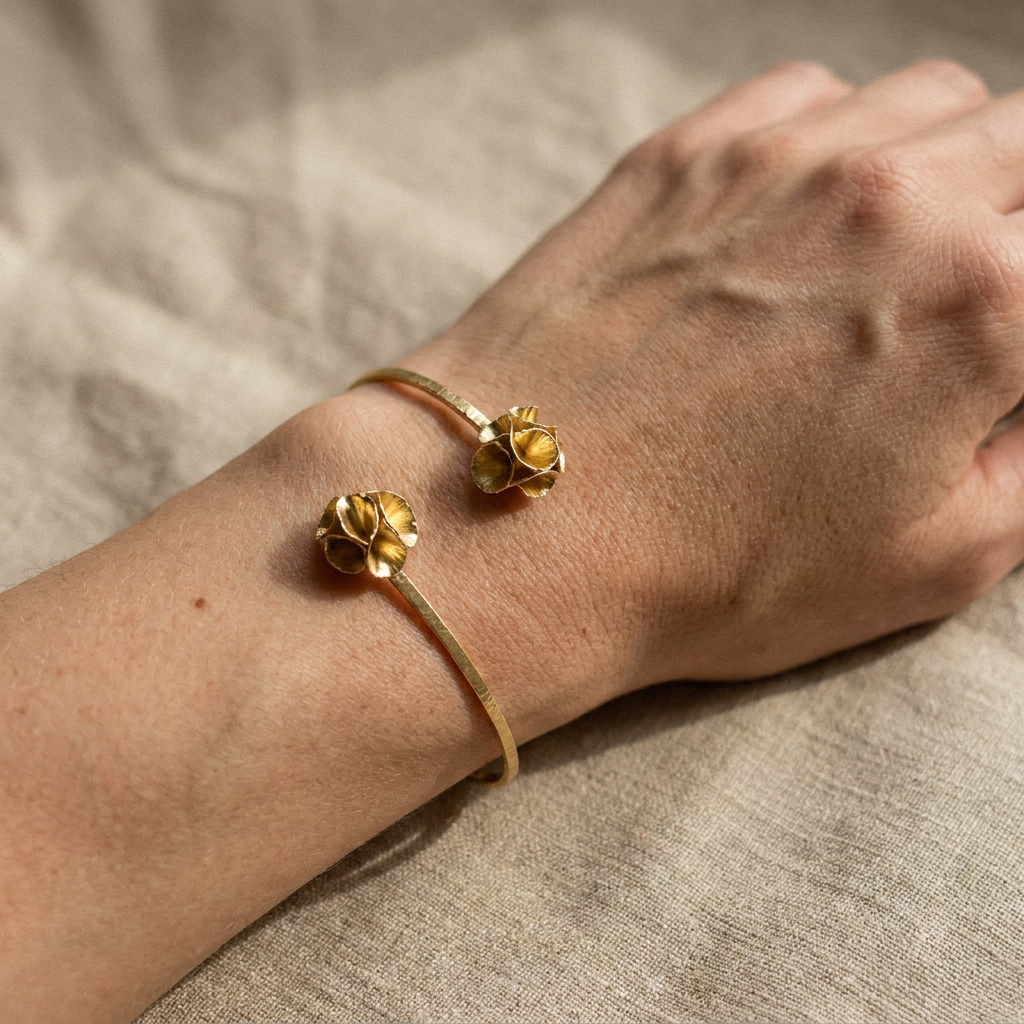 Gold-plated bronze Twin Bloom Bracelet with two sculptural flower ends on a dark stone background.
